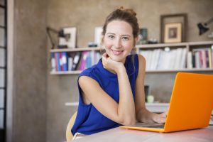 Portrait of young woman with orange laptop sitting in home office